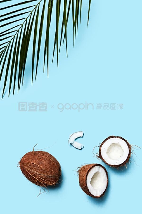 一片椰子和整個椰子,在藍色背景上有一片棕櫚綠葉。食物成分。平鋪。一個由有機的一半和一個椰子組成的美麗組成的藍色背景裝飾著一塊飾板,上面有一片平鋪。